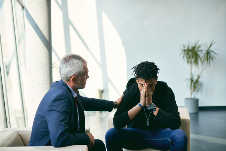 Depressed African American teenager having a meeting with his therapist at psychotherapy center.